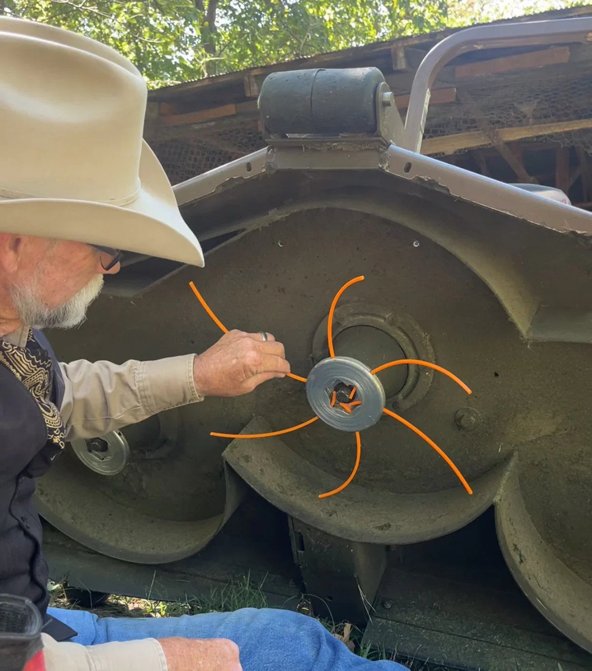 Man installing orange string mower blade alternative on lawn mower deck outdoors